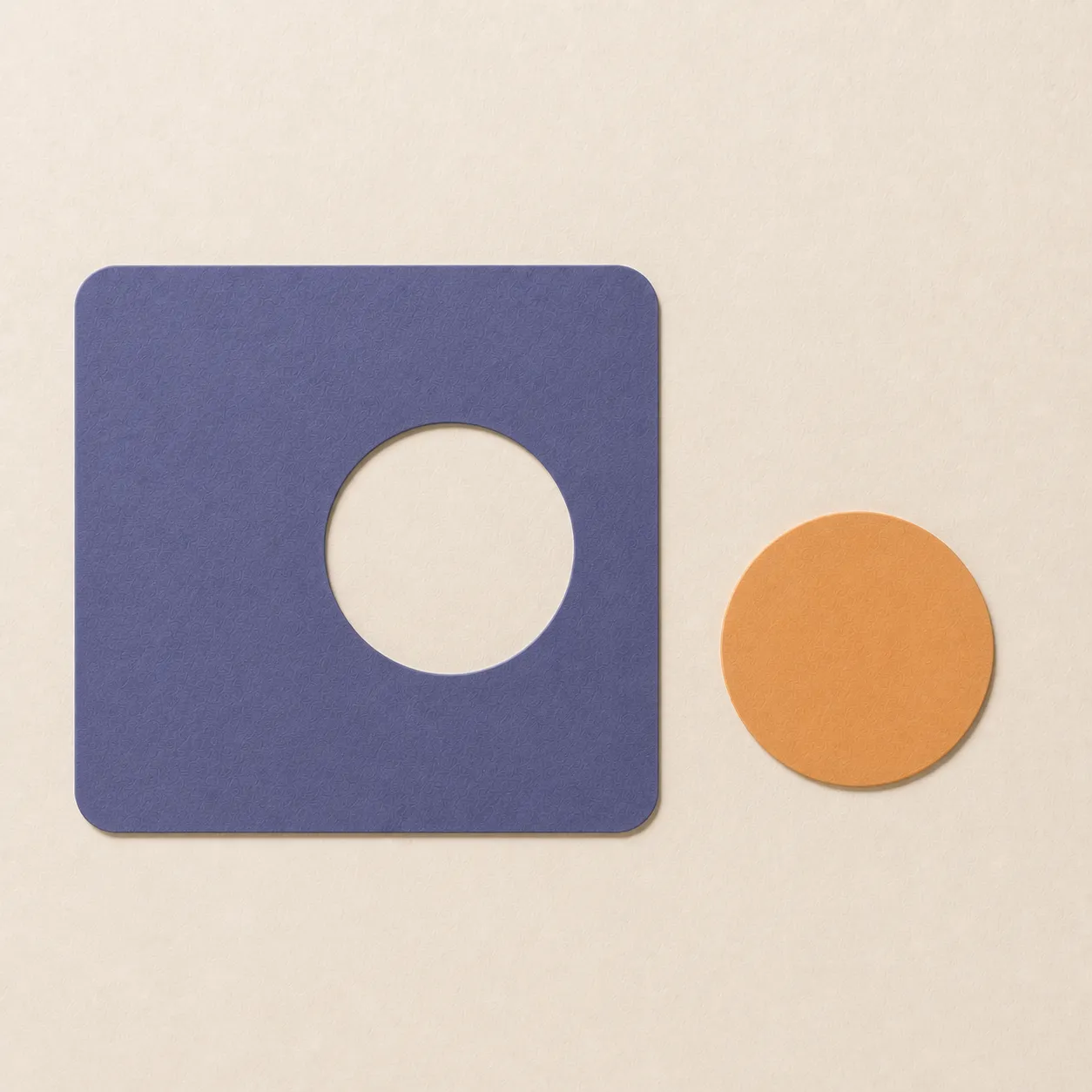 A flat Prelude-indigo paper panel with a circular cutout sits beside the removed apricot disc on a warm ivory surface.
